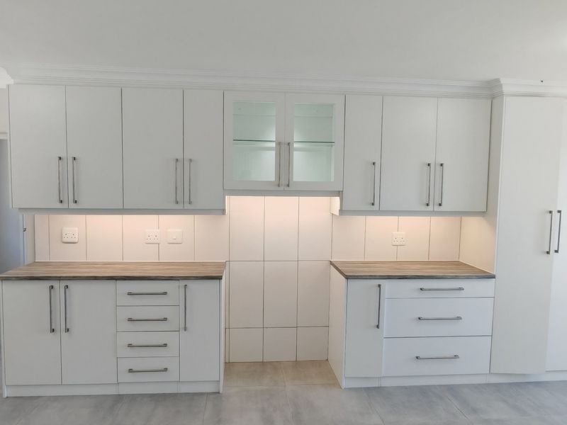 A clean, modern kitchen featuring white built-in cabinetry, wood-look laminate countertops, tiled backsplash, and integrated under-cabinet lighting.