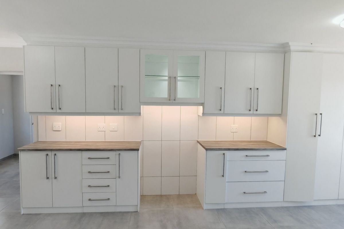 A clean, modern kitchen featuring white built-in cabinetry, wood-look laminate countertops, tiled backsplash, and integrated under-cabinet lighting.