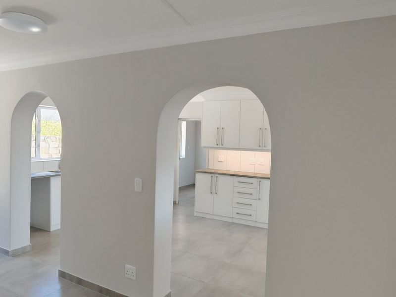 Bright open-plan living area featuring elegant arched doorways, neutral tiled flooring, and a modern kitchen with clean white cabinetry.