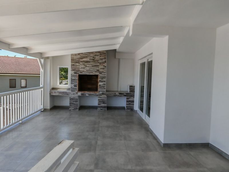 Spacious covered balcony featuring a built-in braai with stone cladding, modern tiled flooring, and direct access to the interior through sliding glass doors.