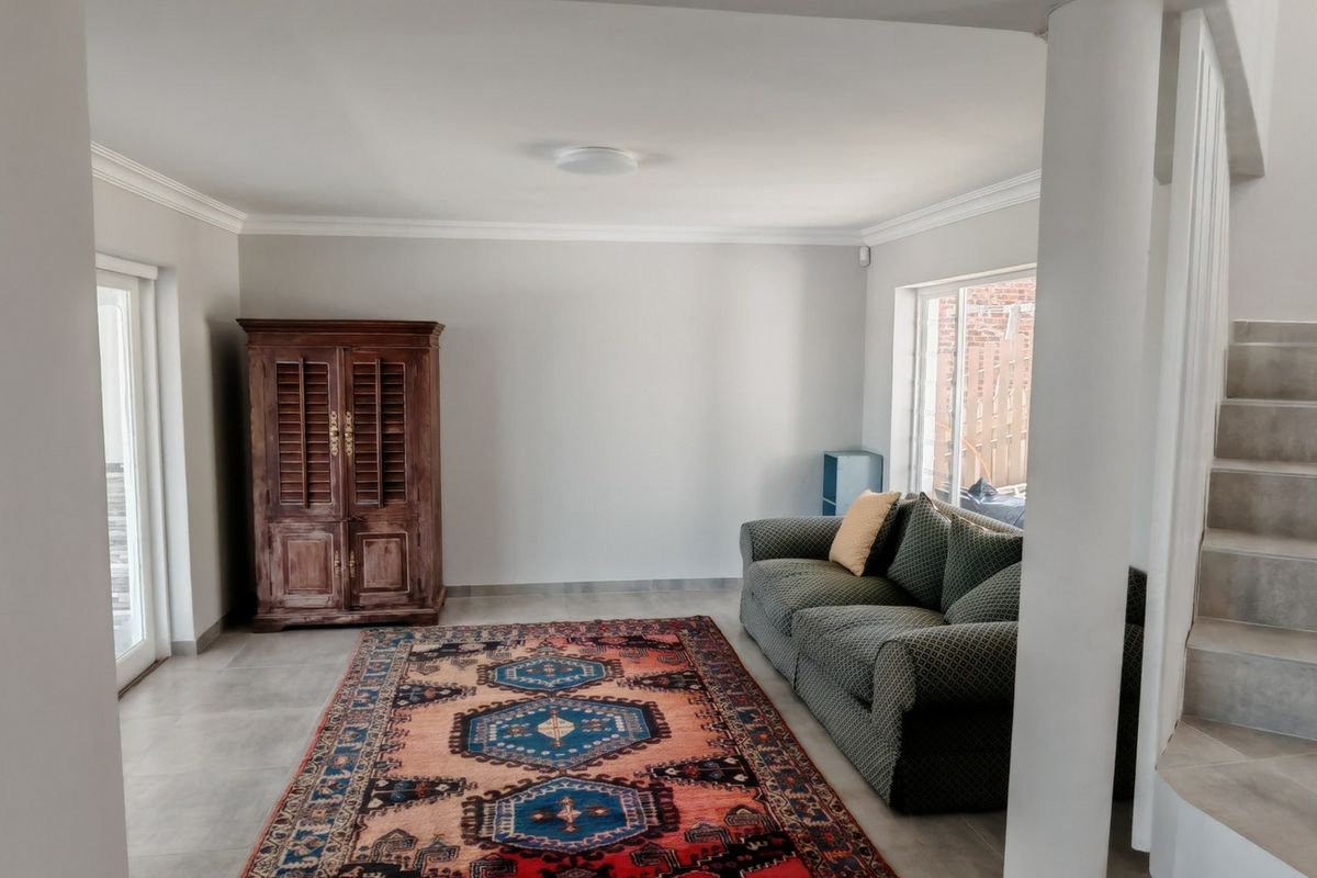 A bright living room featuring neutral tiled flooring, crown molding, and a staircase leading to the upper level.