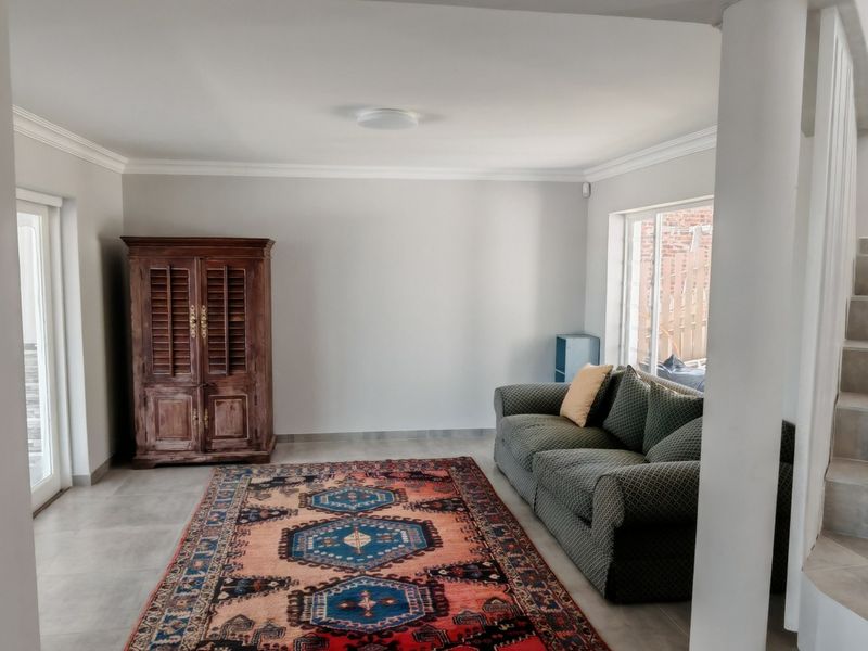 A bright living room featuring neutral tiled flooring, crown molding, and a staircase leading to the upper level.