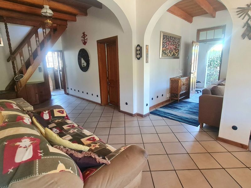 Spacious living area featuring exposed timber ceiling beams, ceramic floor tiles, and classic arched architectural details connecting to the staircase and adjacent rooms.