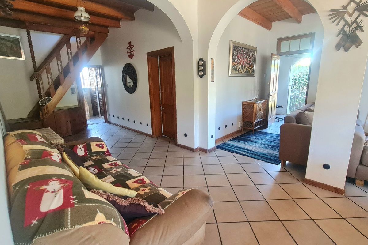 Spacious living area featuring exposed timber ceiling beams, ceramic floor tiles, and classic arched architectural details connecting to the staircase and adjacent rooms.