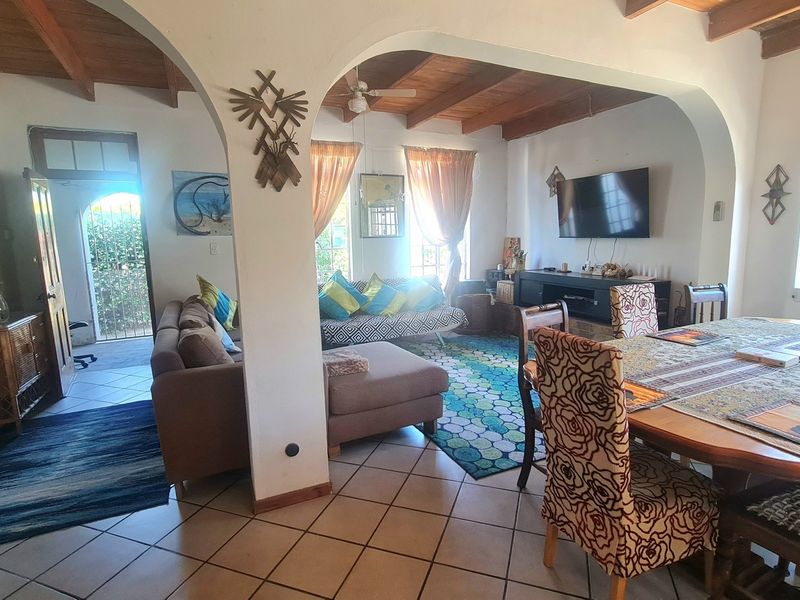 Spacious open-plan living and dining area featuring exposed timber ceiling beams, ceramic floor tiles, and arched architectural transitions between spaces.