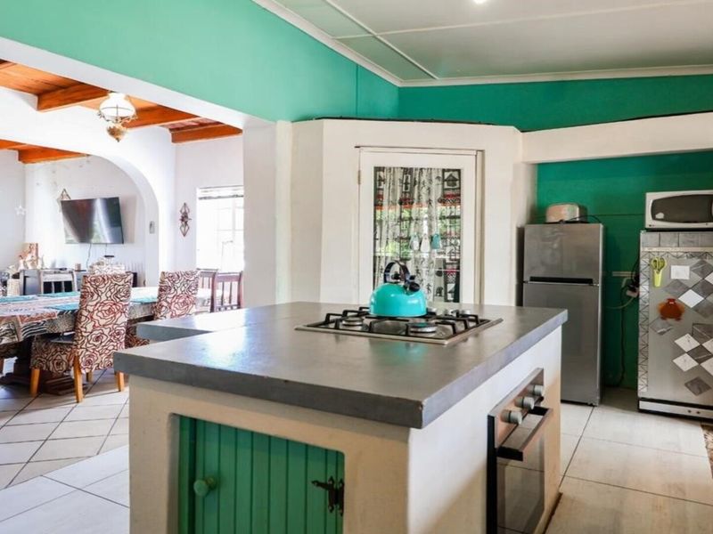 Open-plan kitchen and dining area featuring a central island with built-in hob and oven, exposed timber ceiling beams, and tiled flooring throughout.