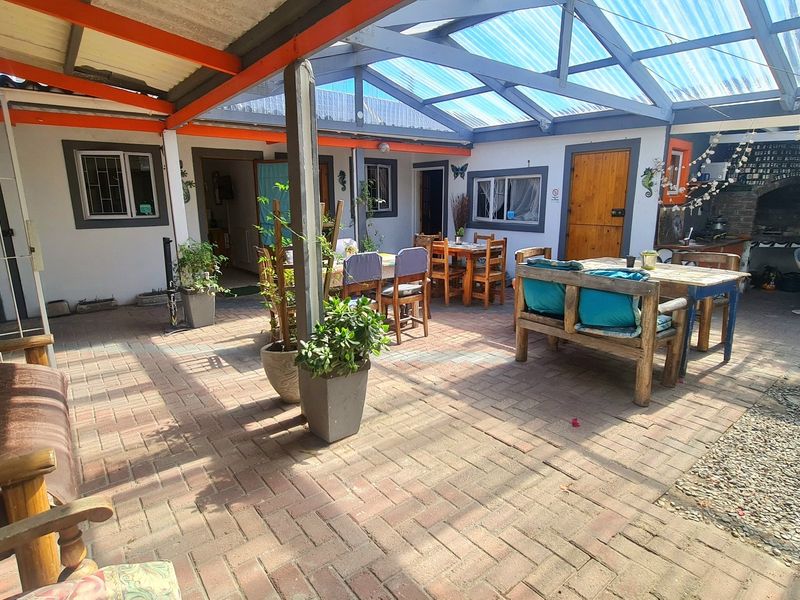 A spacious covered patio area featuring paved flooring, a translucent roof structure, and a built-in brick braai, ideal for outdoor entertaining.