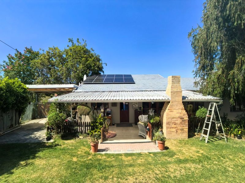 Rear view of the property featuring a covered patio, brick chimney, solar panels on the roof, and a spacious garden area with a carport.