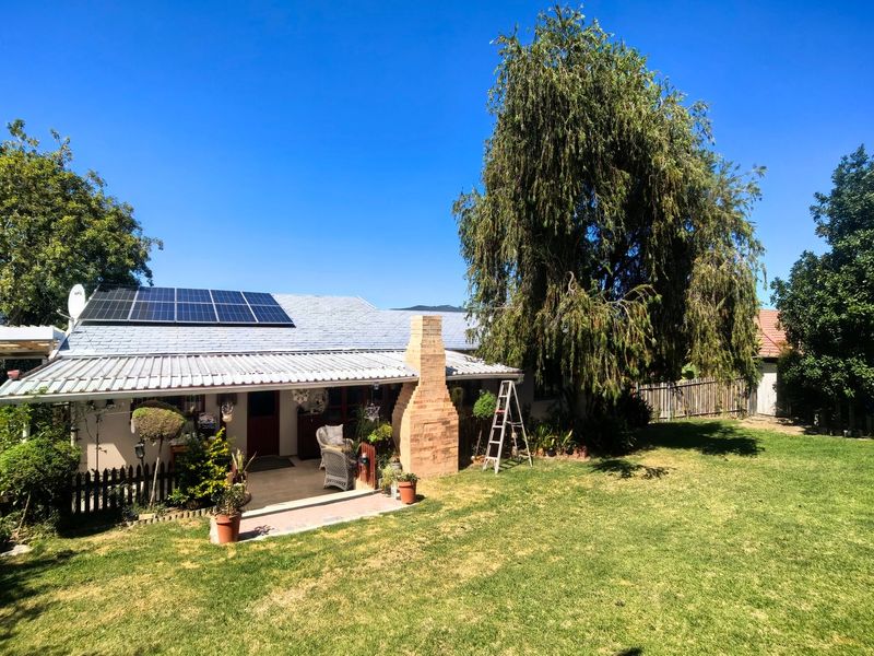 Rear view of the house featuring a covered patio, brick chimney, and roof-mounted solar panels set within a spacious garden.