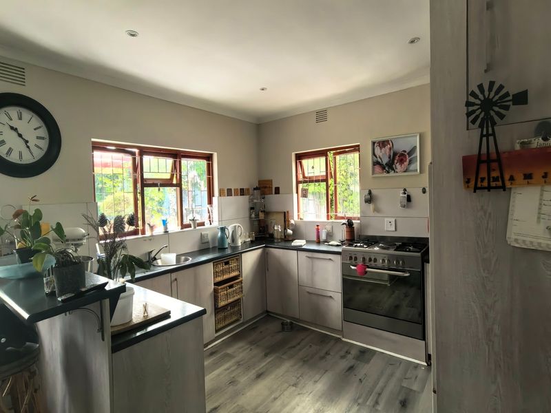 A functional kitchen featuring light-toned cabinetry, dark laminate countertops, a stainless steel stove, and durable laminate flooring with ample natural light.