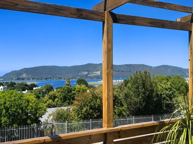 Elevated outdoor view featuring a timber pergola and railing, overlooking lush greenery, a lagoon, and distant mountains.