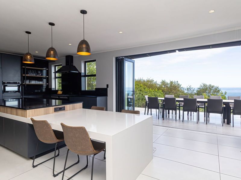Modern open-plan kitchen featuring a large island, premium built-in appliances, and seamless indoor-outdoor flow through bi-fold doors to a scenic patio.