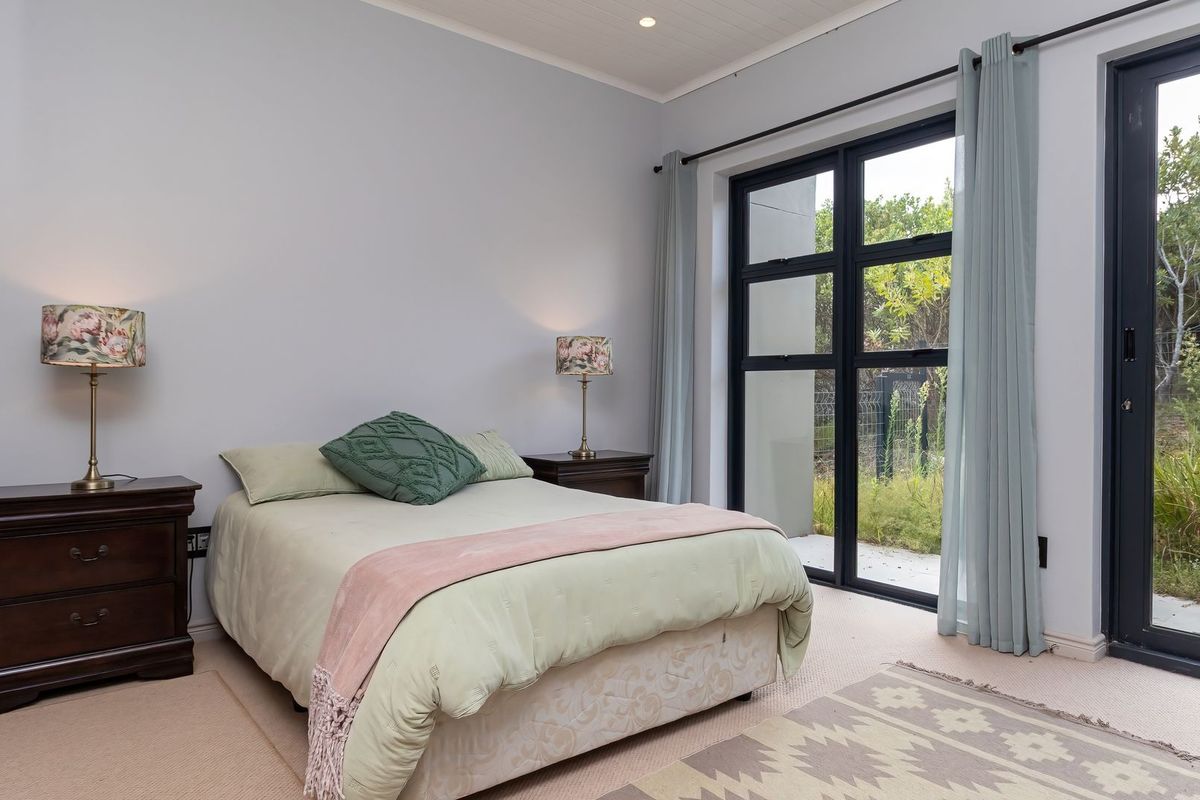 A well-maintained bedroom featuring neutral carpeting, tongue and groove ceiling detail, and large black aluminium sliding doors providing direct access to the garden.