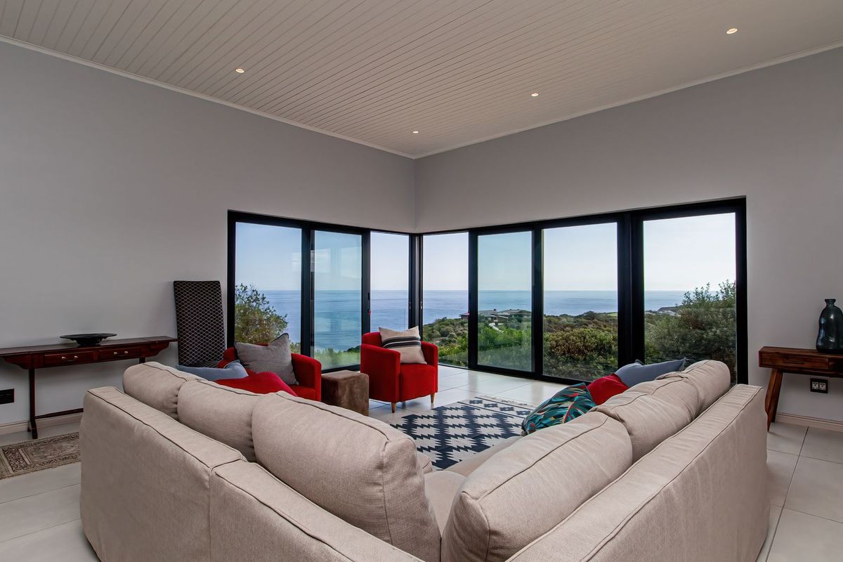 Spacious living room featuring high tongue and groove ceilings, tiled floors, and expansive corner sliding glass doors offering panoramic ocean views.