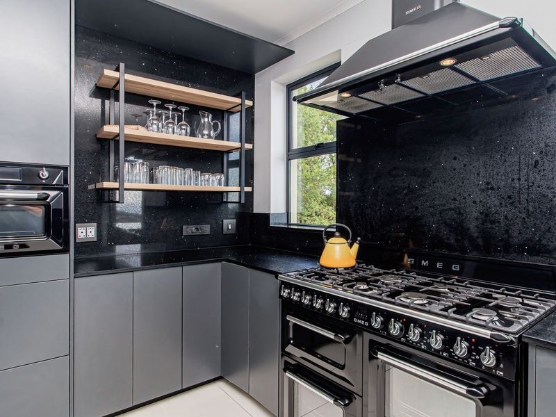 Modern kitchen featuring sleek grey cabinetry, black stone countertops, high-end Smeg appliances, and open shelving.