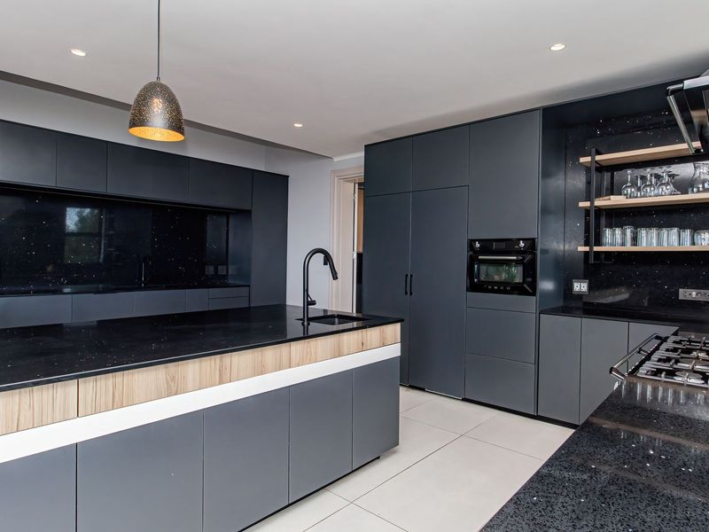 Modern kitchen featuring dark cabinetry, a large central island with stone countertops, integrated appliances, gas hob, and sleek contemporary finishes.