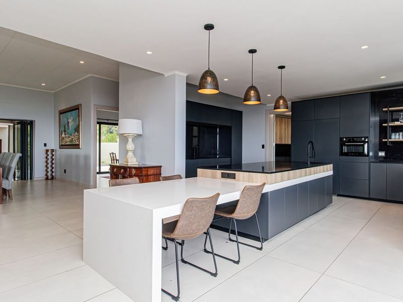 Modern open-plan kitchen featuring a large central island, sleek dark cabinetry, integrated appliances, and contemporary pendant lighting, flowing into an adjacent dining area.