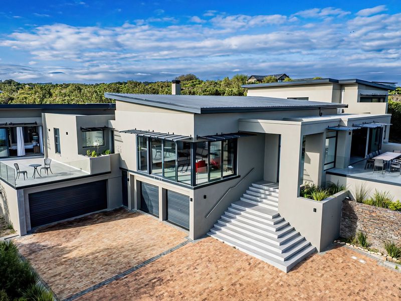 Modern multi-level architectural home featuring a paved driveway, double garage, expansive glass windows, and elevated outdoor patio areas with contemporary stone and concrete finishes.