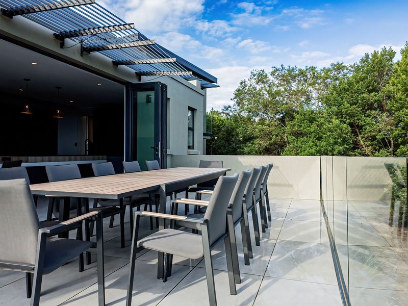 Spacious outdoor balcony featuring modern tiled flooring, a sleek glass balustrade, and a louvred pergola, seamlessly connected to the interior via folding stacker doors.