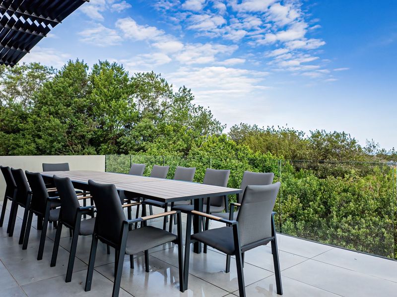 Spacious outdoor patio featuring modern tiled flooring, a sleek glass balustrade, and a louvred roof, offering a seamless transition to the surrounding greenery.