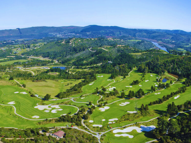 An expansive aerial view of a lush, well-maintained golf course set within a scenic landscape of rolling hills and natural vegetation.