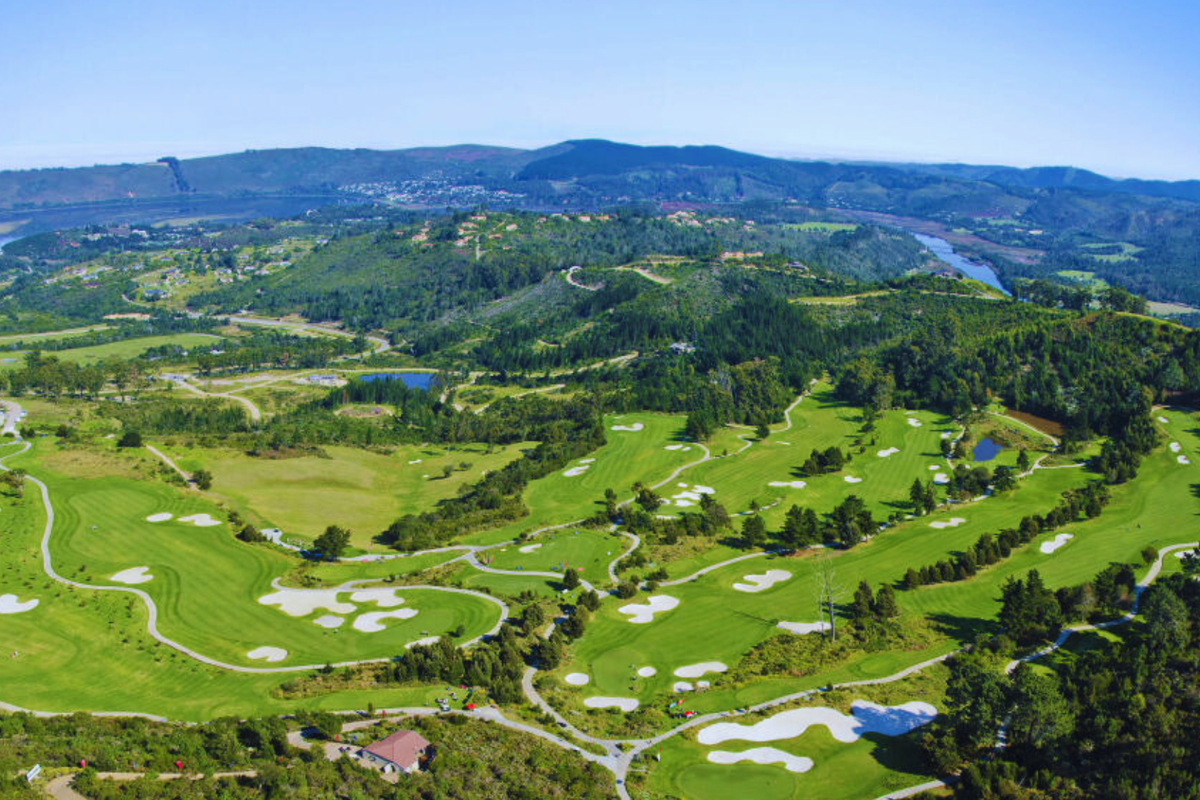 An expansive aerial view of a lush, well-maintained golf course set within a scenic landscape of rolling hills and natural vegetation.