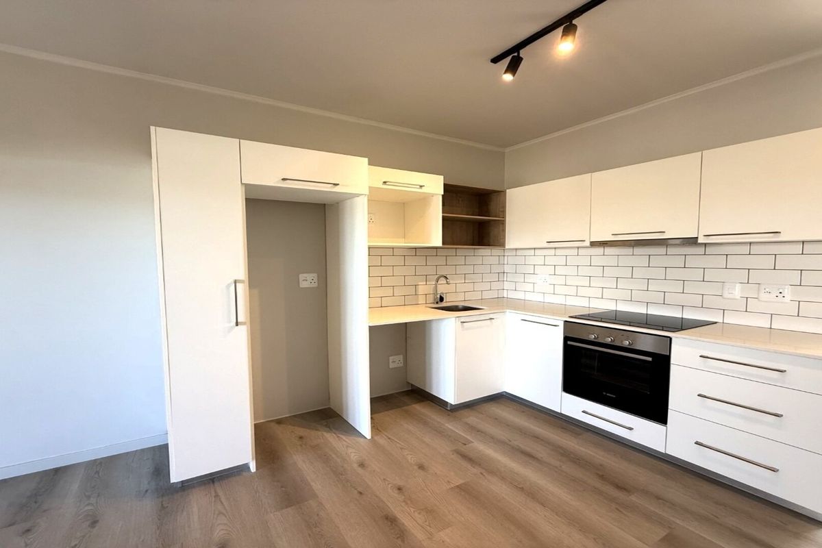 Modern kitchen featuring white cabinetry, subway tile backsplash, integrated electric oven and hob, and wood-look laminate flooring in an open-plan layout.