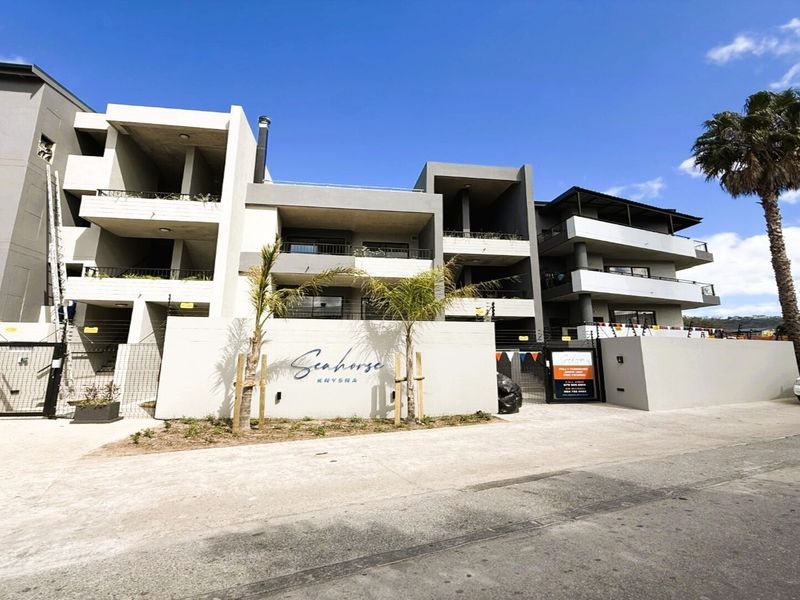 Modern apartment complex exterior featuring contemporary concrete architecture, private balconies, secure gated entrance, and electric fencing.