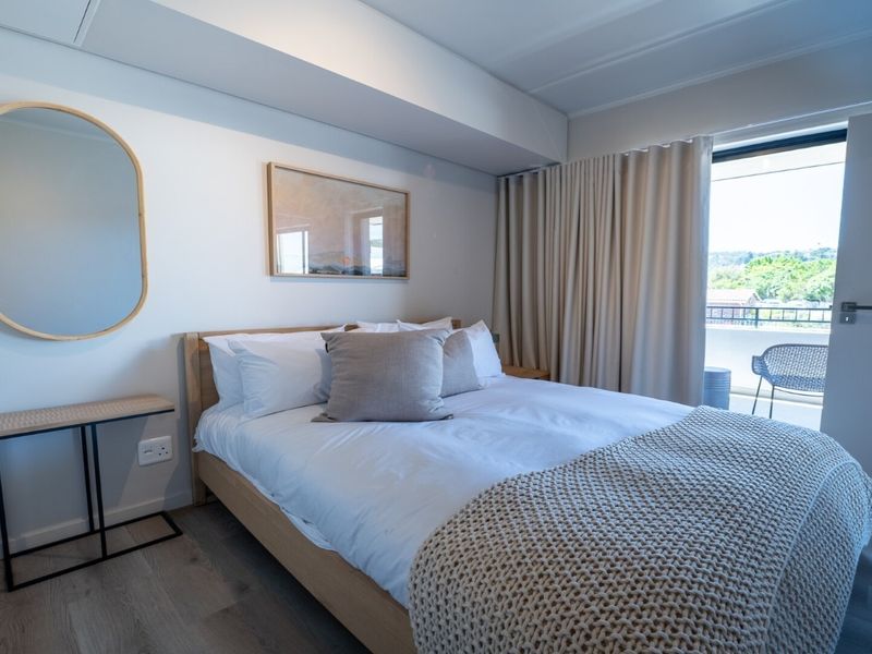 A well-maintained bedroom featuring light laminate flooring and direct access to a private balcony through a sliding glass door.