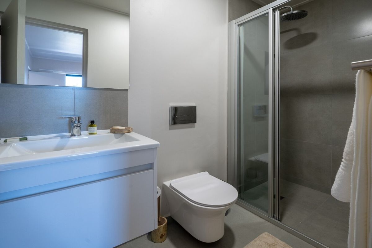 Modern bathroom featuring a wall-hung toilet, vanity with basin, and a glass-enclosed shower with neutral grey tiling.