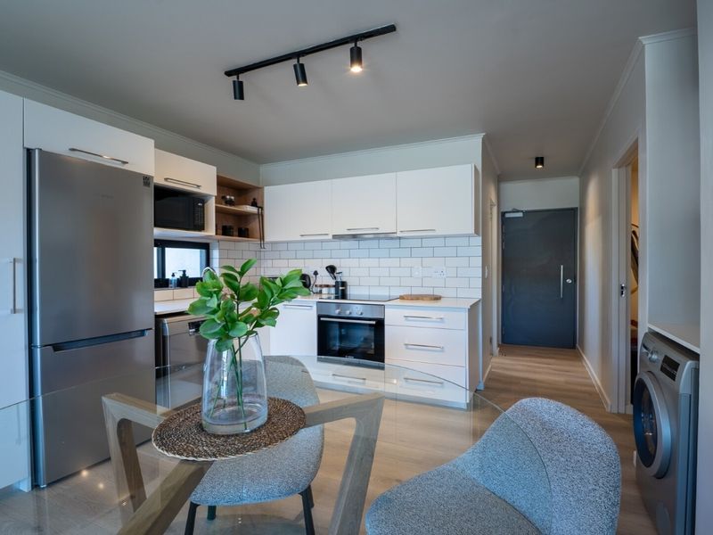Modern open-plan kitchen featuring white cabinetry, subway tile backsplash, integrated appliances, and track lighting, seamlessly flowing into the living area.