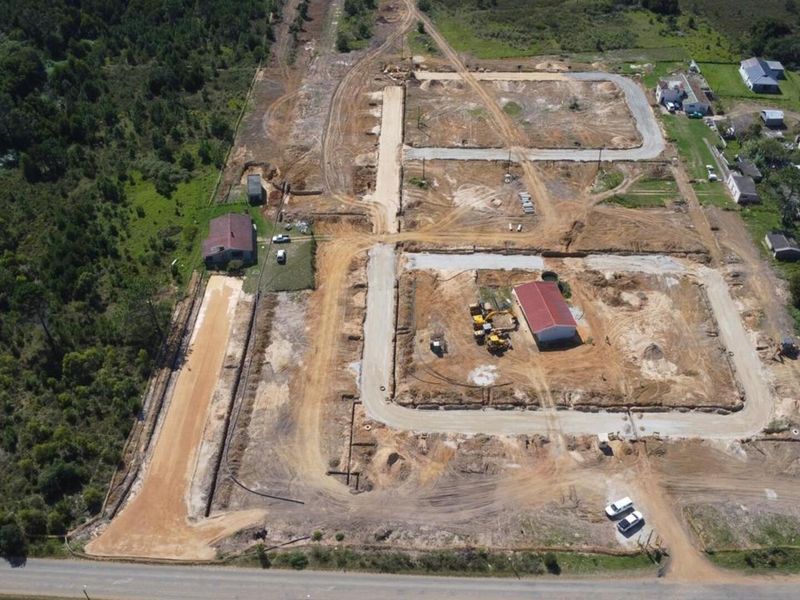 Aerial view of a residential development site showing cleared land, road infrastructure, and existing structures in progress.