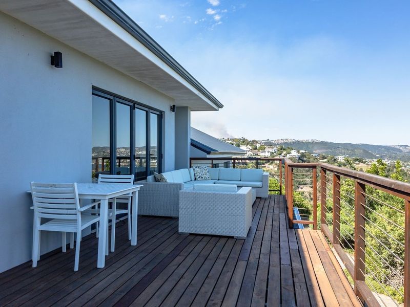 Spacious elevated balcony featuring timber decking and stainless steel cable railings, offering expansive views of the surrounding landscape and water.