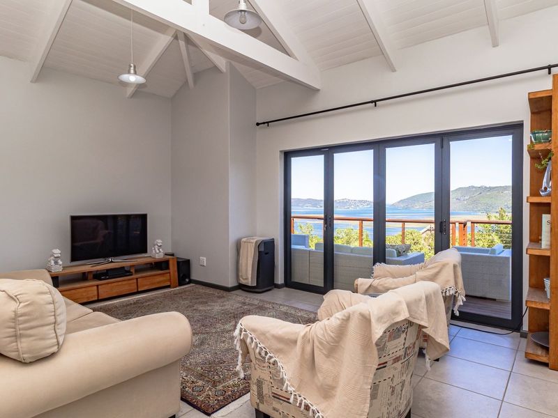 Spacious living room featuring vaulted ceilings with exposed rafters, tiled flooring, and large bi-fold doors opening to a scenic balcony with water views.