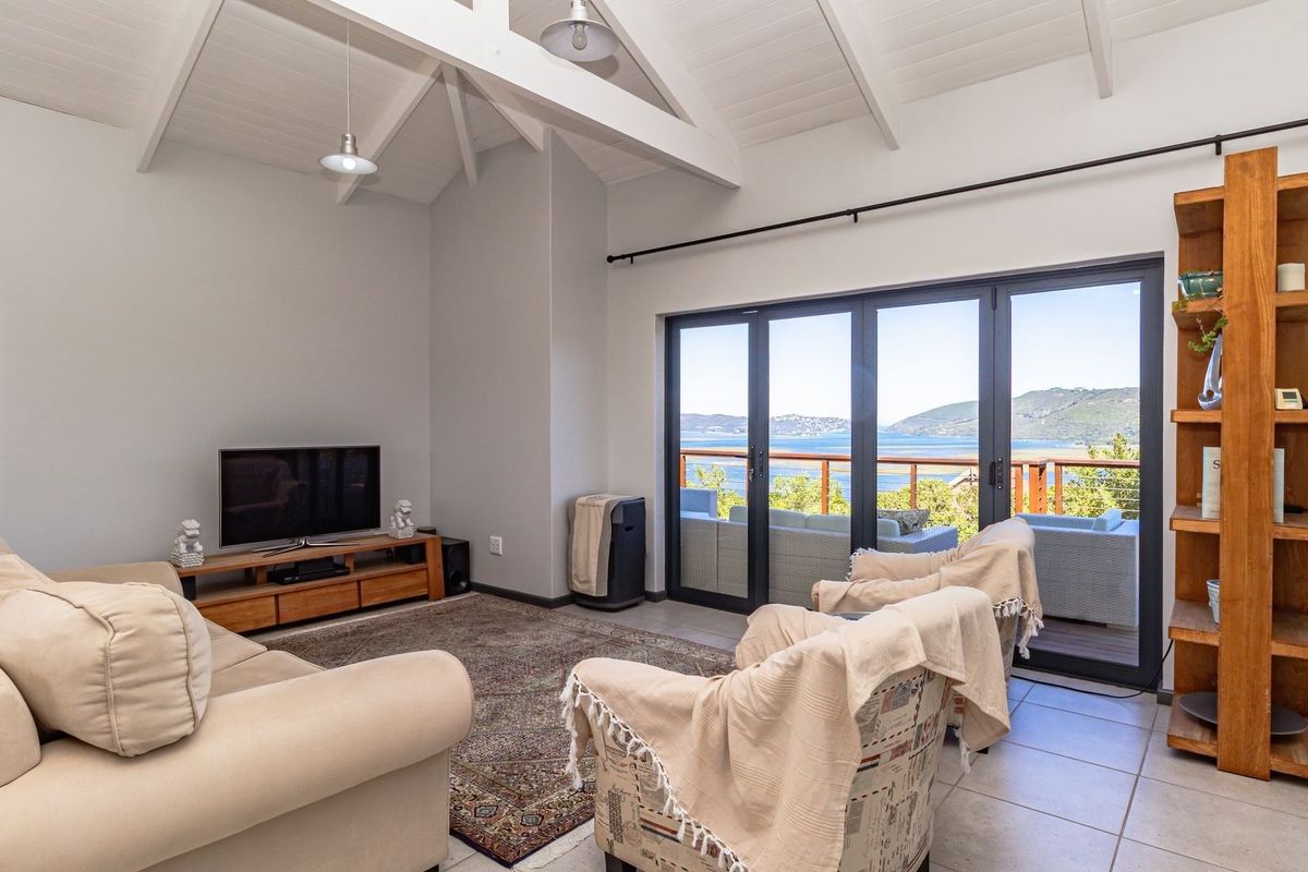 Spacious living room featuring vaulted ceilings with exposed rafters, tiled flooring, and large bi-fold doors opening to a scenic balcony with water views.