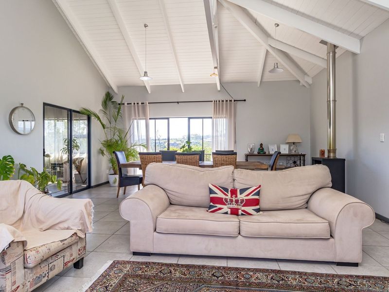 Spacious open-plan living and dining area featuring a high vaulted timber ceiling, tiled floors, and a modern freestanding fireplace with large sliding glass doors.