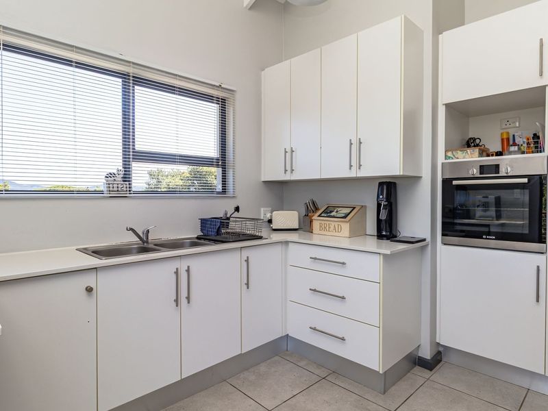 A functional kitchen featuring white cabinetry, a built-in oven, stainless steel sink, and tiled flooring with natural light from the window.