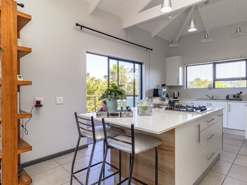 Modern kitchen featuring a central island with a gas hob, sleek white cabinetry, vaulted ceilings with exposed beams, and direct access to an outdoor deck.