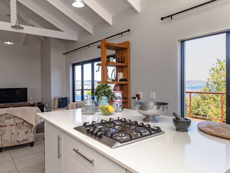 Spacious open-plan living area featuring a modern kitchen island with gas cooktop, vaulted ceilings with exposed beams, and large sliding doors with scenic views.