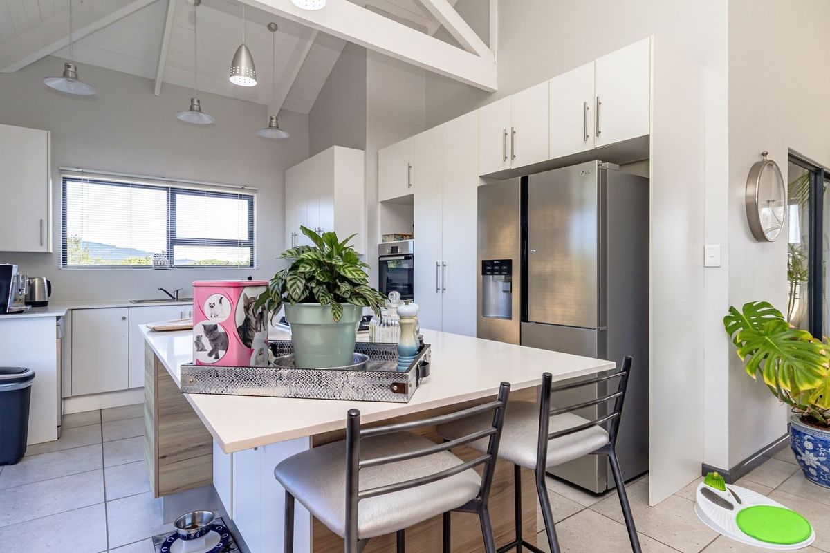 Modern kitchen featuring a central island, sleek white cabinetry, stainless steel appliances, and a high vaulted ceiling with pendant lighting.