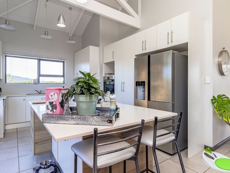 Modern kitchen featuring a central island, sleek white cabinetry, stainless steel appliances, and a high vaulted ceiling with pendant lighting.