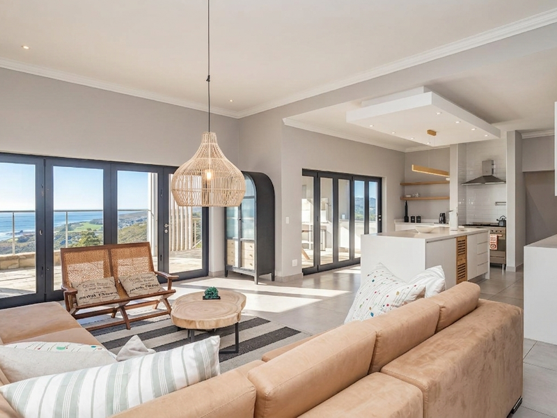 Spacious open-plan living area featuring a modern kitchen with an island, sleek finishes, and large sliding doors opening to a scenic coastal view.
