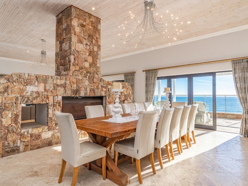 Spacious dining area featuring a prominent stone fireplace, timber-clad ceiling, and large sliding doors opening to an ocean view.