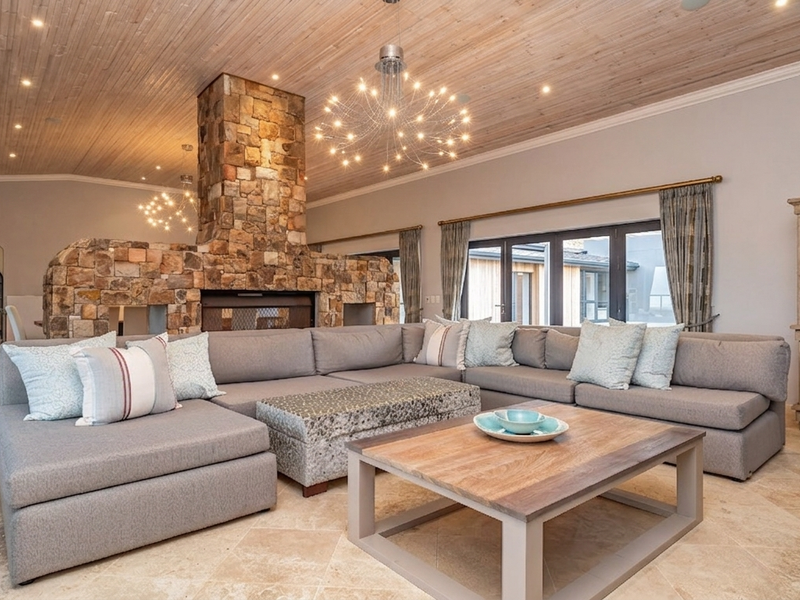 Spacious living room featuring a prominent stone fireplace, elegant timber-clad ceiling, and high-quality travertine flooring with direct access to the exterior through french doors.