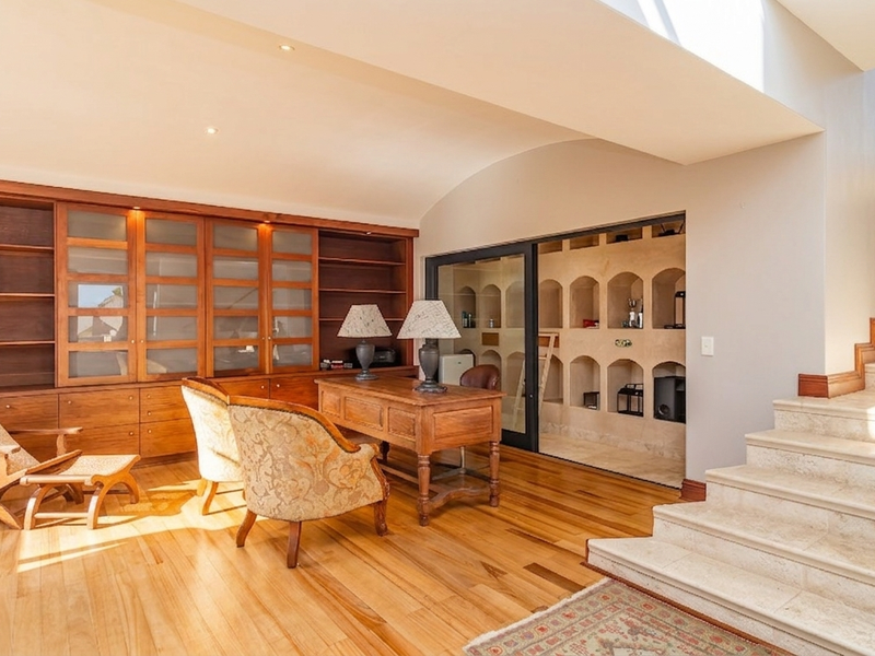 A spacious home office featuring extensive built-in wooden cabinetry, a stone staircase, and unique recessed display shelving with integrated lighting.