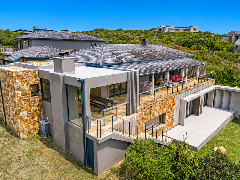 Aerial view of the rear elevation featuring stone cladding, a spacious tiled patio, a balcony with glass balustrades, and an external staircase.