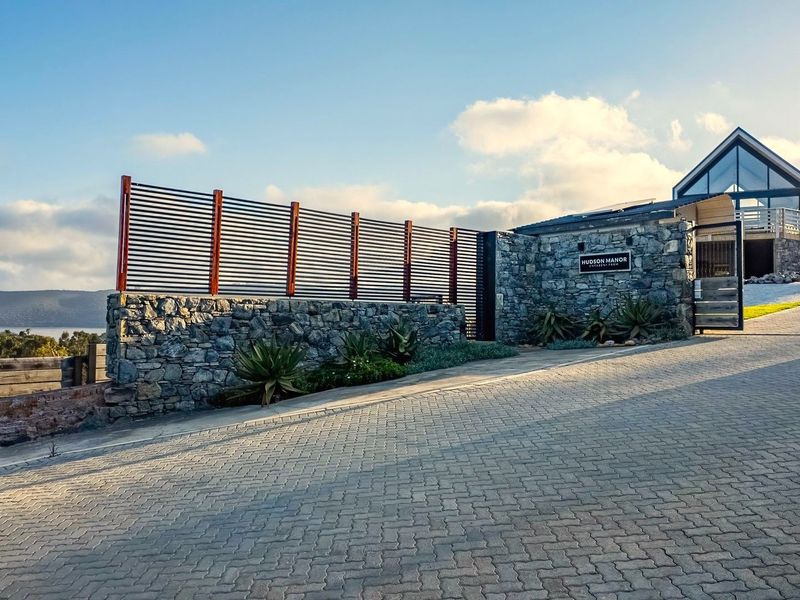 A modern residential entrance featuring a stone boundary wall, slatted privacy screening, and a paved driveway leading to a contemporary architectural structure.