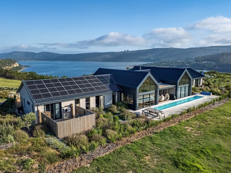 Aerial view of a modern residential property featuring a metal roof with solar panels, a swimming pool, and expansive views of the surrounding landscape.