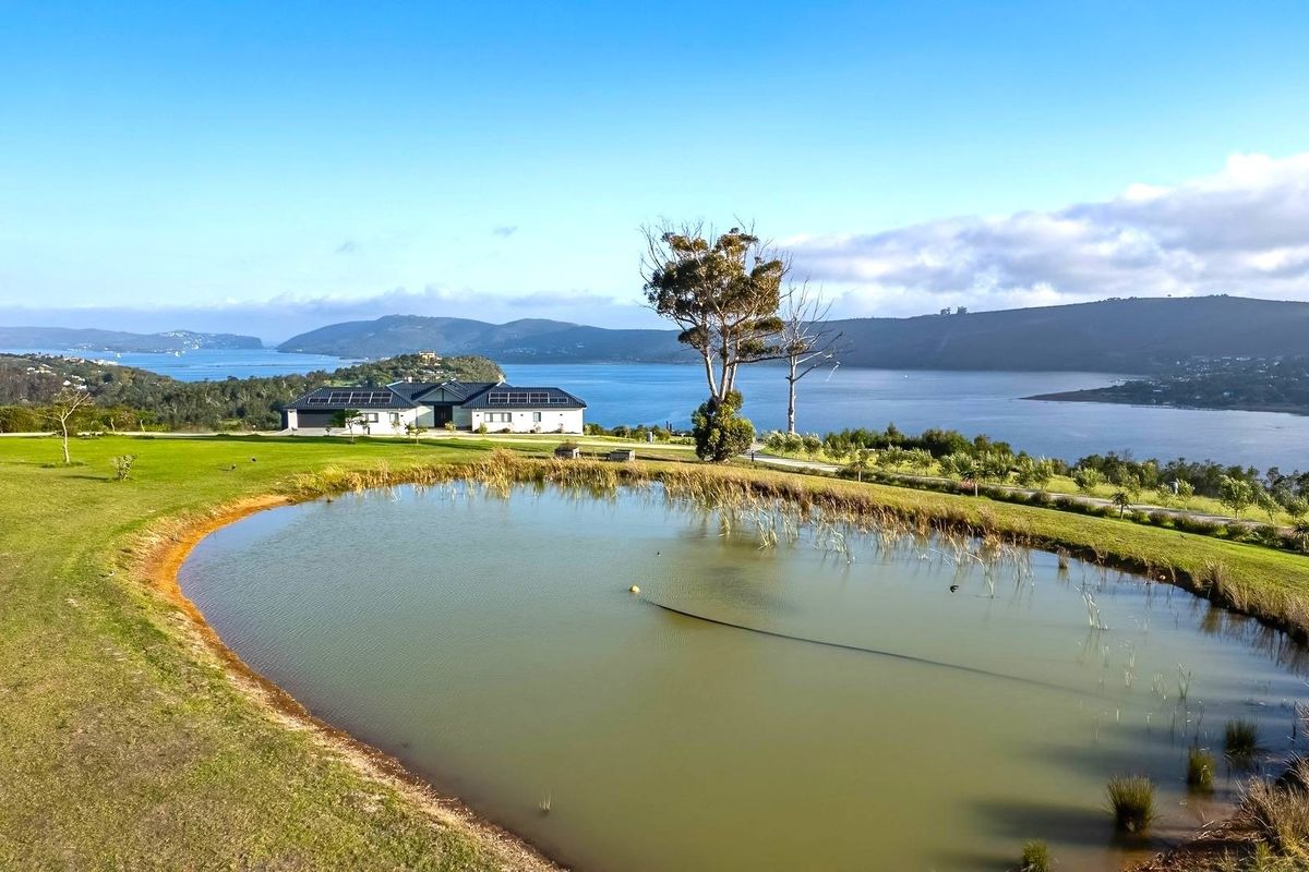 Aerial view of a residential property featuring a large pond, landscaped grounds, and solar panels, overlooking a scenic estuary and mountain landscape.