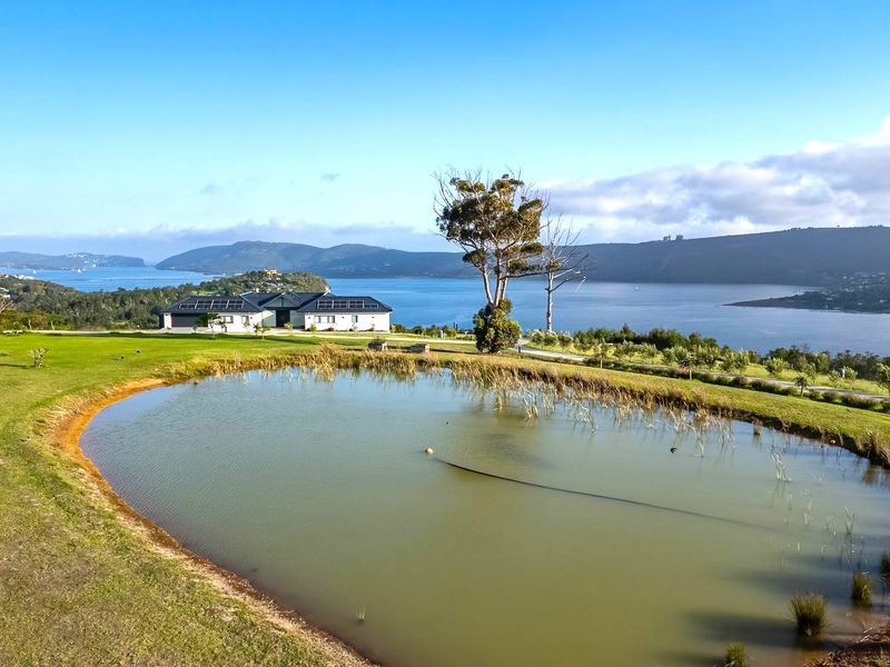 Aerial view of a residential property featuring a large pond, landscaped grounds, and solar panels, overlooking a scenic estuary and mountain landscape.